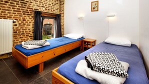 Una habitación con dos camas de madera, una pared de ladrillo, una ventana con cortinas y una pequeña mesa.