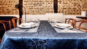 Una mesa de comedor con platos, vasos y cubiertos, frente a una pared de ladrillo con un reloj.