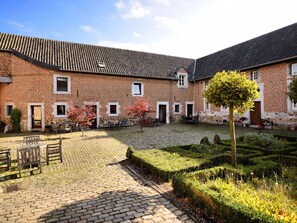 A courtyard with a brick building, outdoor seating, and a well-maintained garden. - Nice apartments in a monumental square farm. (Richelle)