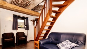 A living room with a dark blue leather sofa, two brown armchairs, a wooden staircase, and a window with curtains. - Lovely Holiday Home in Richelle with Barbecue (Richelle)