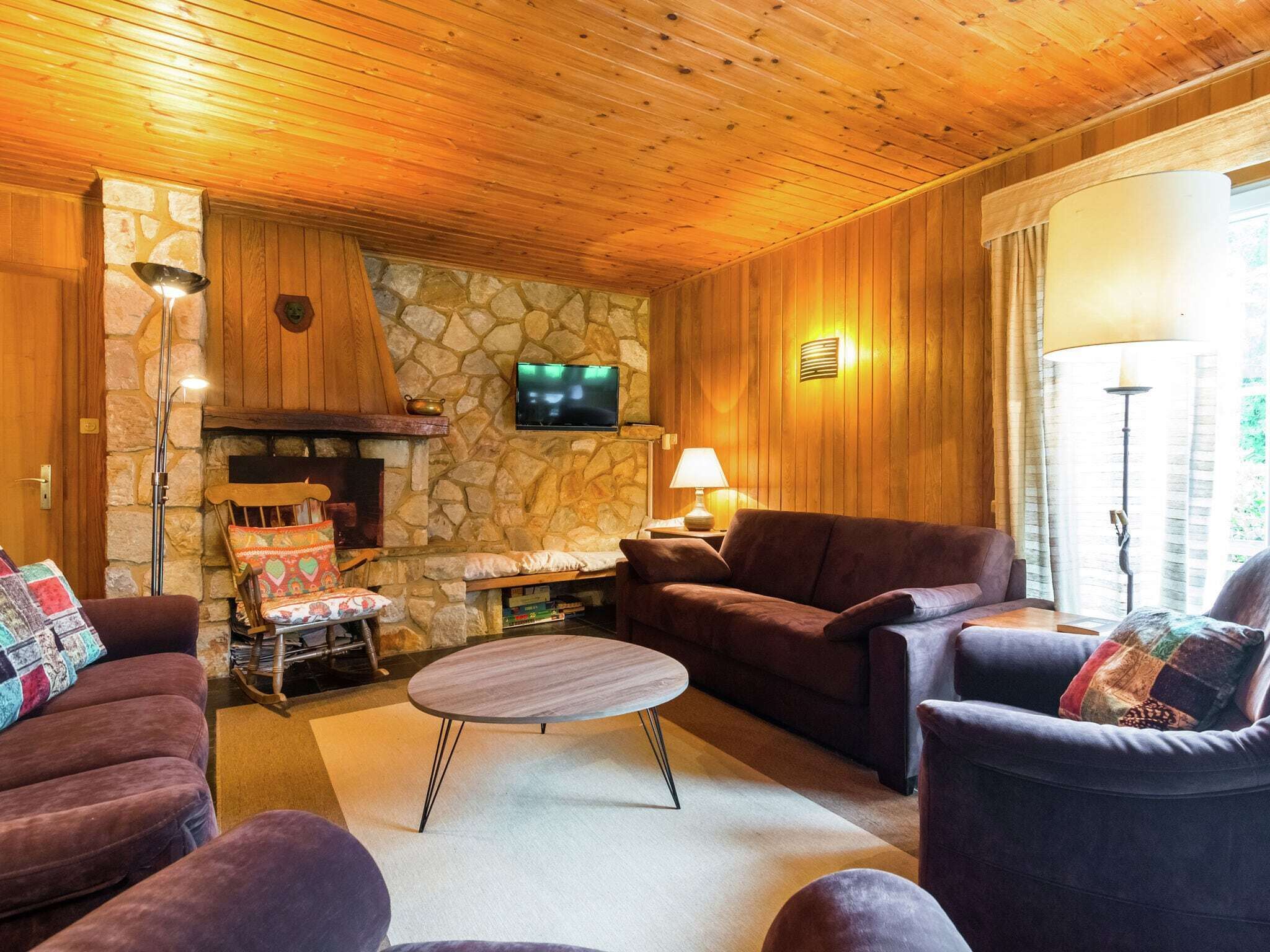A cozy living room with wooden walls, a stone fireplace, and comfortable seating.