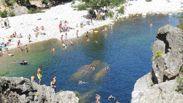 Ein felsiger Flussufer mit badenden und sonnenden Personen.