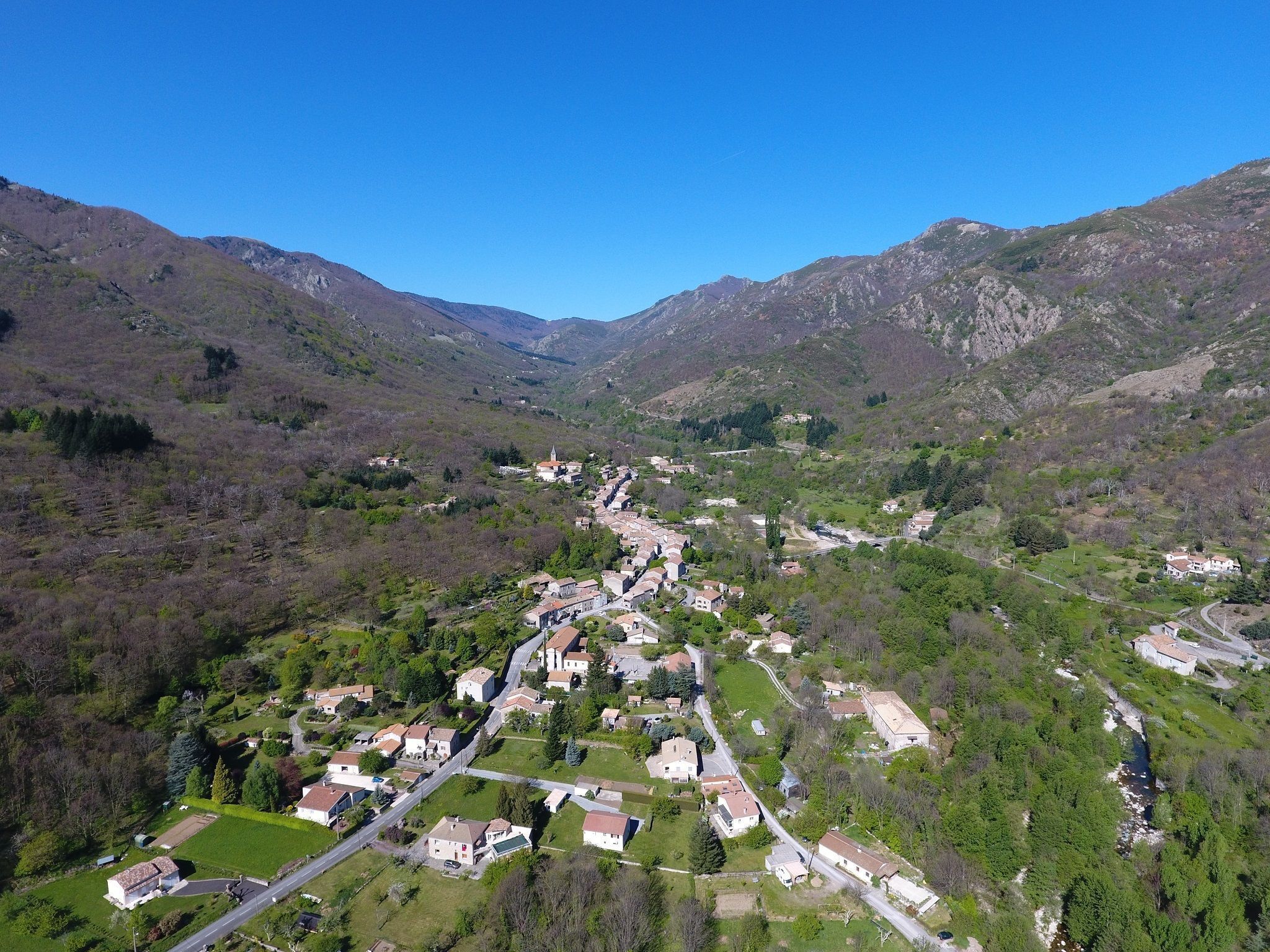 A mountainous village with houses and a church, surrounded by greenery and hills.