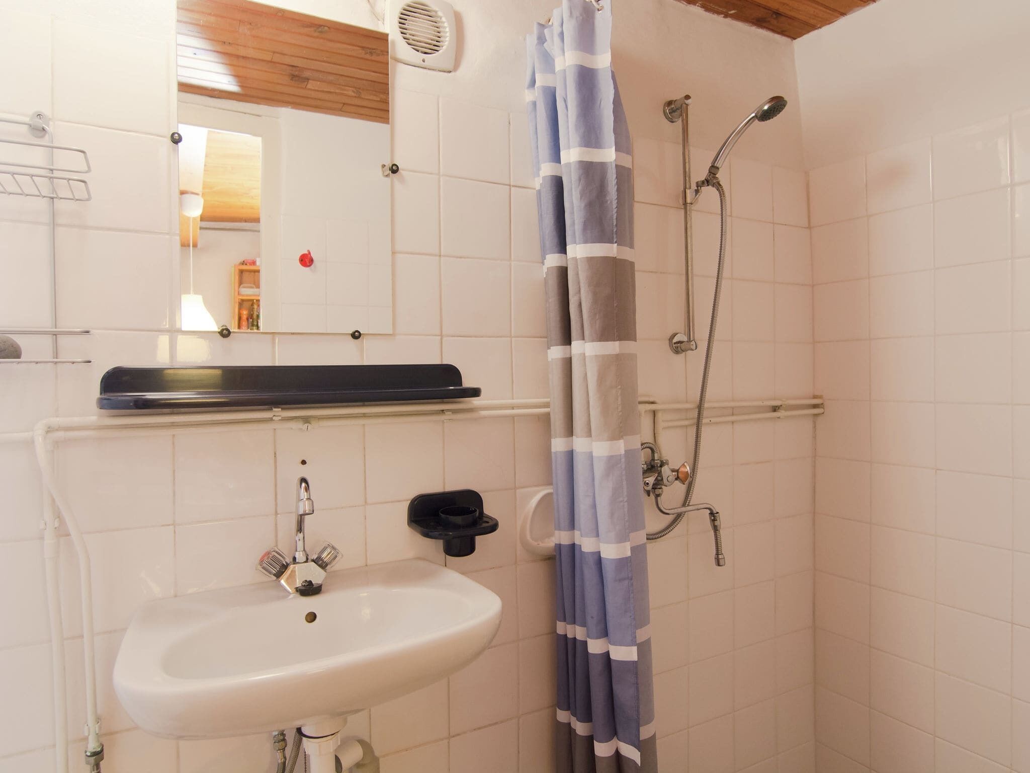 Een badkamer met een wit wastafel, een spiegel, een douche met een blauw-grijs gestreept douchegordijn en een houten plafond.