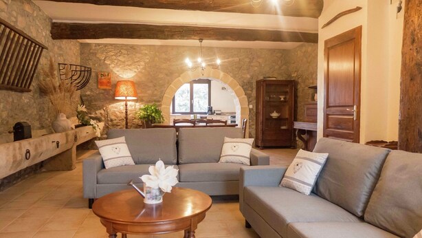 A cozy living room with a stone wall, a wooden ceiling, and a dining area in the background. - Cottage in Montbrun-des-Corbières (Montbrun des Corbières)
