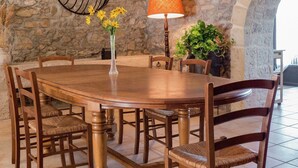 A round wooden dining table with six chairs, a vase with yellow flowers, a wall-mounted black metal light fixture, and a lamp with an orange lampshade. - Cottage in Montbrun-des-Corbières (Montbrun des Corbières)