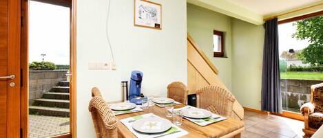 A dining area with a wooden table set for two, wicker chairs, a coffee maker, and a framed picture on the wall.
