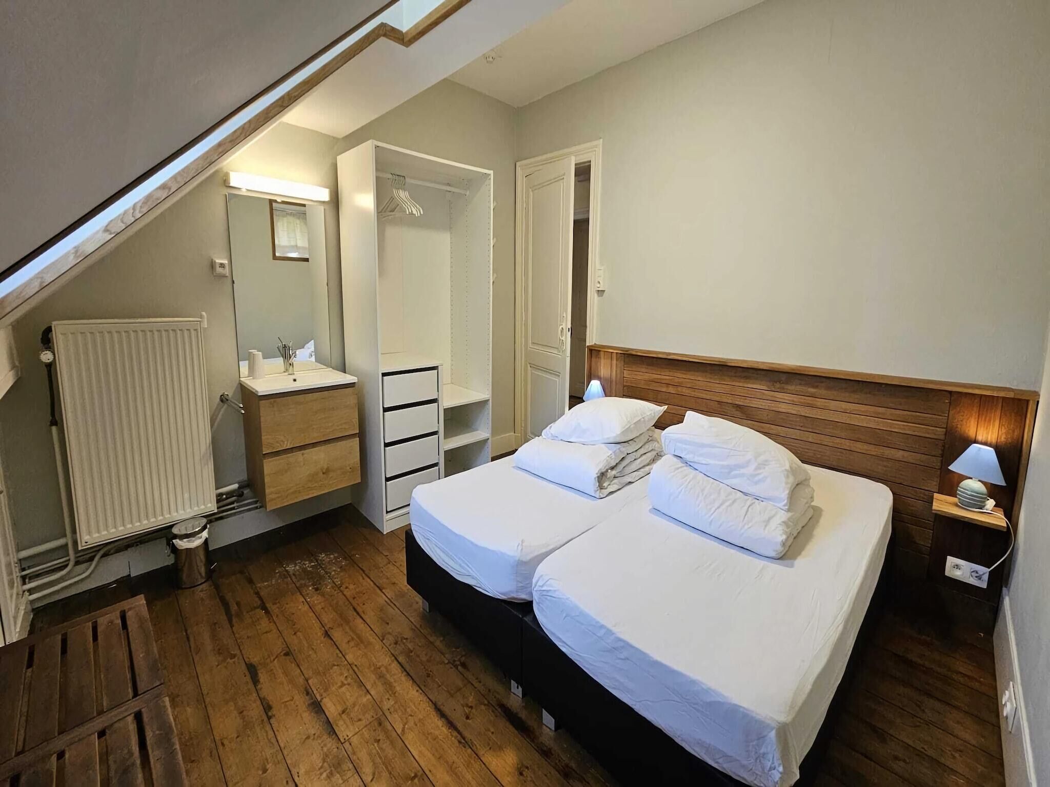 Ein Schlafzimmer mit zwei Betten, einem begehbaren Kleiderschrank, einem Heizkörper, einem Waschbecken und einem Nachttisch mit Lampe.