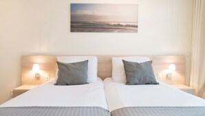 Habitación de hotel con dos camas, cada una con una almohada y una mesita de noche con lámpara.