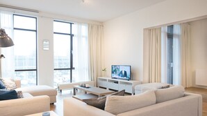 Una sala moderna con sofá, mesa de centro y televisor sobre un mueble blanco.