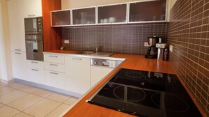 A modern kitchen with white cabinets, a built-in oven, a sink, and a black induction cooktop.
