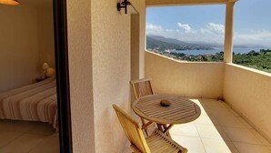 A balcony with a view of a coastal landscape, a round wooden table, and two wooden chairs.