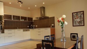 A modern kitchen with white cabinets, a tiled backsplash, and a dining area with a glass table and black chairs.