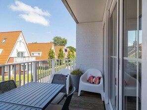 Een balkon met een tafel en stoelen, een bloempot en uitzicht op omliggende huizen.
