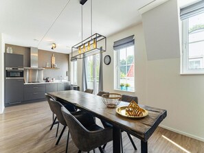 A modern kitchen with built-in appliances, a dining area with a wooden table and chairs, and a large window providing natural light. - Luxury apartment in Koudekerke with sauna (Koudekerke)