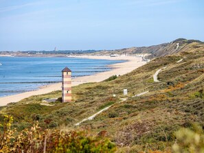 A coastal landscape with a lighthouse, beach, and hilly terrain.