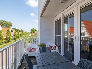 A balcony with a table and chairs, a white railing, and a view of neighboring houses. - Luxury apartment in Koudekerke with sauna (Koudekerke)