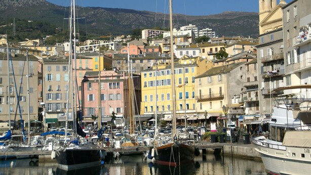 A marina with boats docked, surrounded by colorful buildings and a church with two domes. - Apartment in Corsica near Beaches (Poggio Mezzana)
