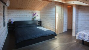 A bedroom with a wooden ceiling, a bed with a dark bedspread, a nightstand with a lamp, and a small table with a vase of flowers. - Apartment in Corsica near Beaches (Poggio Mezzana)