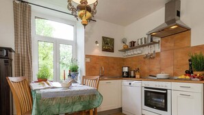 Una cocina con mesa de comedor, sillas, cafetera, estufa y ventana con cortinas.