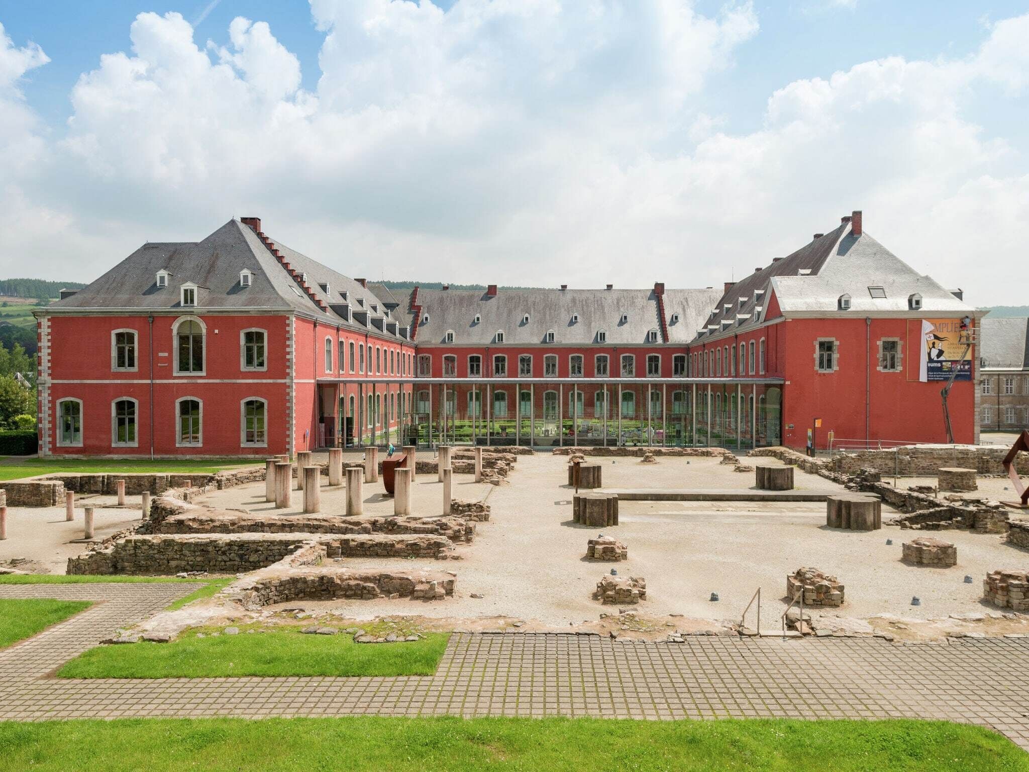 A historic building with a symmetrical facade, large windows, and a courtyard with ruins.