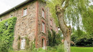 Un edificio de piedra con detalles en ladrillo rojo, ventanas grandes y un árbol en primer plano.