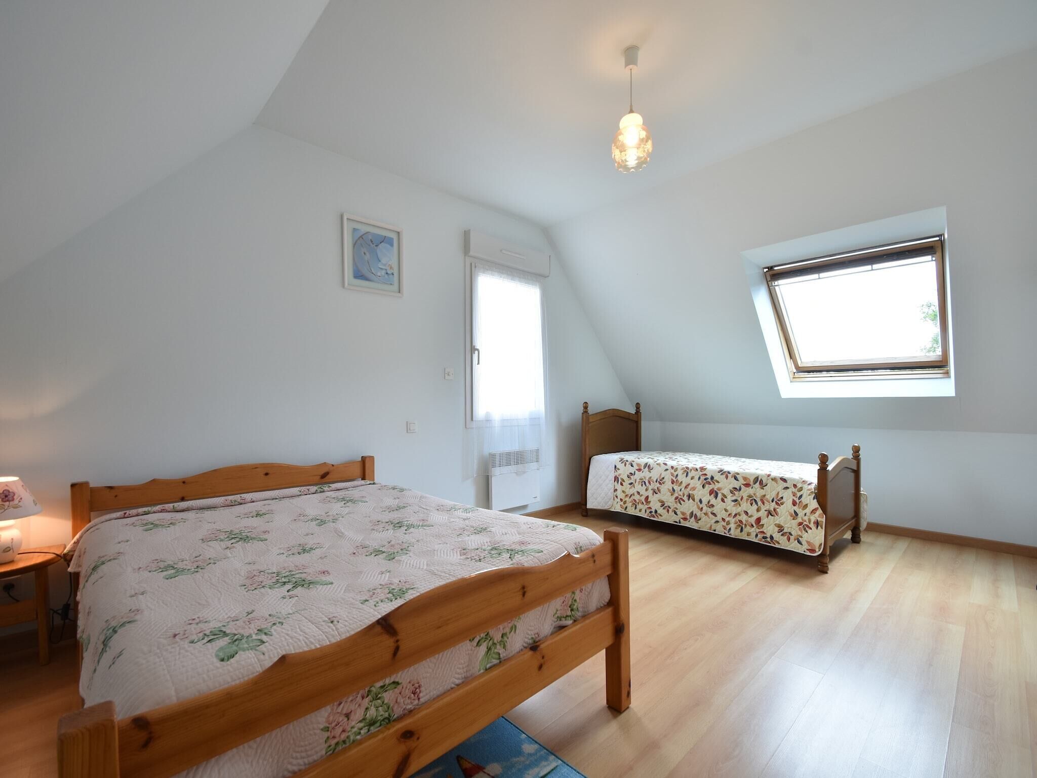 A bedroom with two wooden beds, a skylight, a window, and a ceiling light.