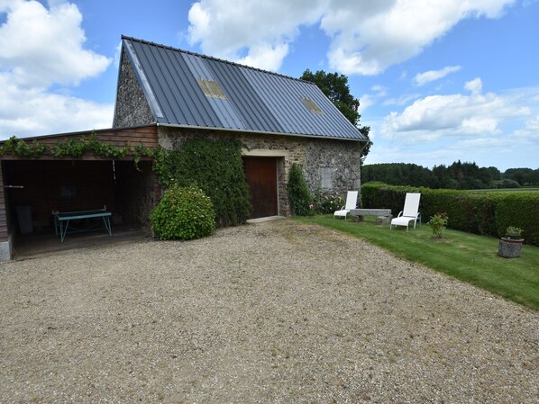 A stone barn with a gravel driveway, a covered garage, and a seating area with white chairs.