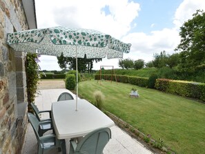 An outdoor patio with a table and chairs, a patterned umbrella, and a well-maintained lawn with a swing set in the background. - Home for 7 Guests in Plouvara (Plouvara)
