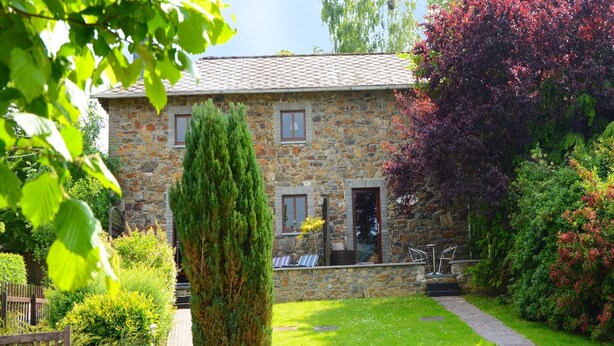A stone house with a well-maintained garden, a tall coniferous tree, and a brick pathway leading to the entrance.