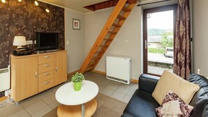 A living room with a TV, wooden cabinet, and a small table with a plant.