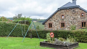 A stone house with a sloped roof, a swing set, and a no parking sign in the yard.