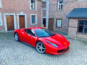 A red sports car parked in front of a brick building with multiple doors and windows. - Historic Hideaway in Exbomont (Stoumont)