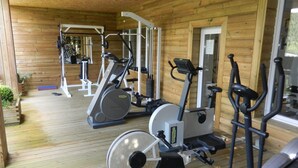 Een overdekte gymruimte met diverse fitnessapparaten, waaronder loopbanden en hometrainers, in een houten chaletachtige omgeving.