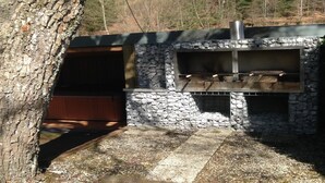 A stone-built outdoor kitchen with a grill and a chimney, surrounded by a forested area. - Holiday Home in Borgoumont near Spa Town (La Gleize)