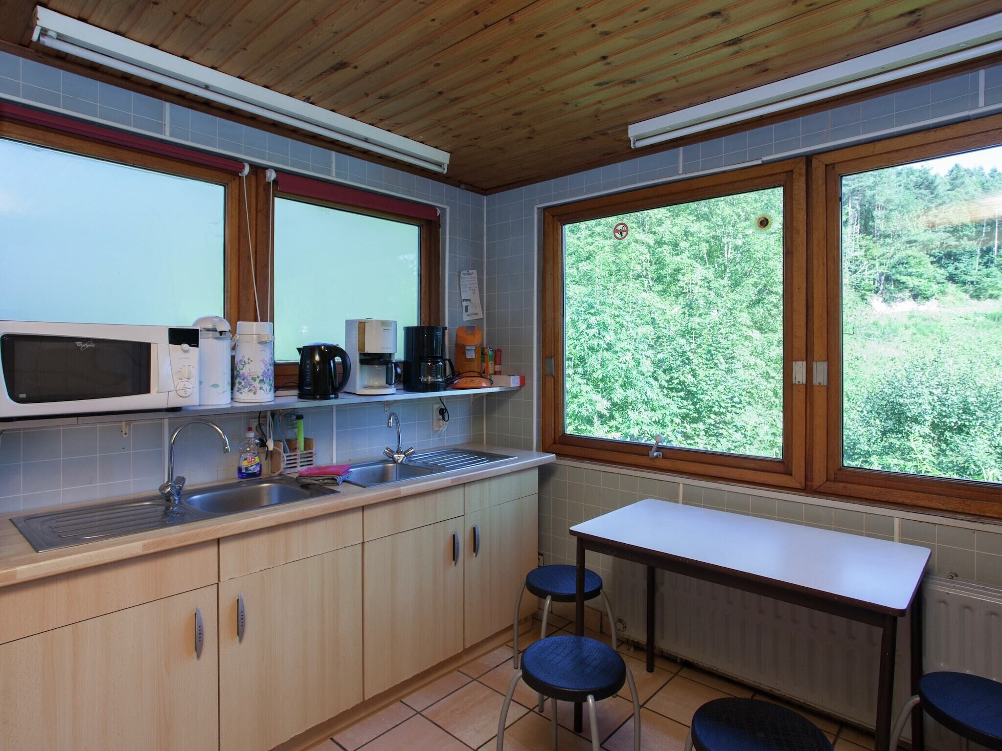 Une cuisine compacte équipée d’un four à micro-ondes, d’une machine à café et d’un évier. Une fenêtre offre une vue sur la verdure environnante.