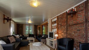 A cozy living room with a brick wall, a wooden coffee table, and a television. - Holiday Home in Borgoumont near Spa Town (La Gleize)