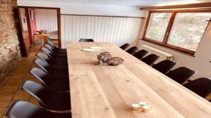 A long wooden table with black chairs, a stone wall, and a window with a view of trees. - Holiday Home in Borgoumont near Spa Town (La Gleize)