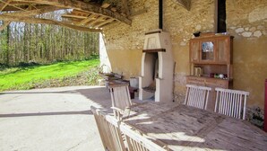 Ein Holztisch mit Stühlen steht draußen unter einem Steinhaus mit rustikalem Inneren.