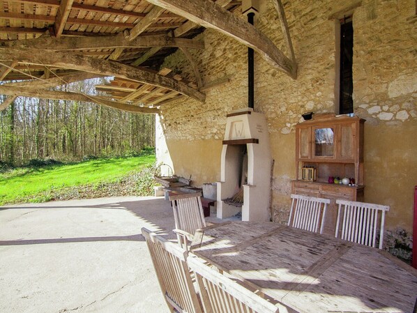 An outdoor wooden table and chairs under a stone building with a rustic interior.