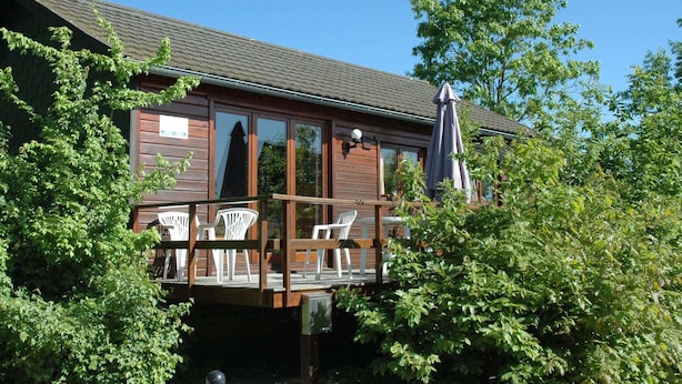 Een houten chalet met een balkon, witte plastic stoelen en een tafel.