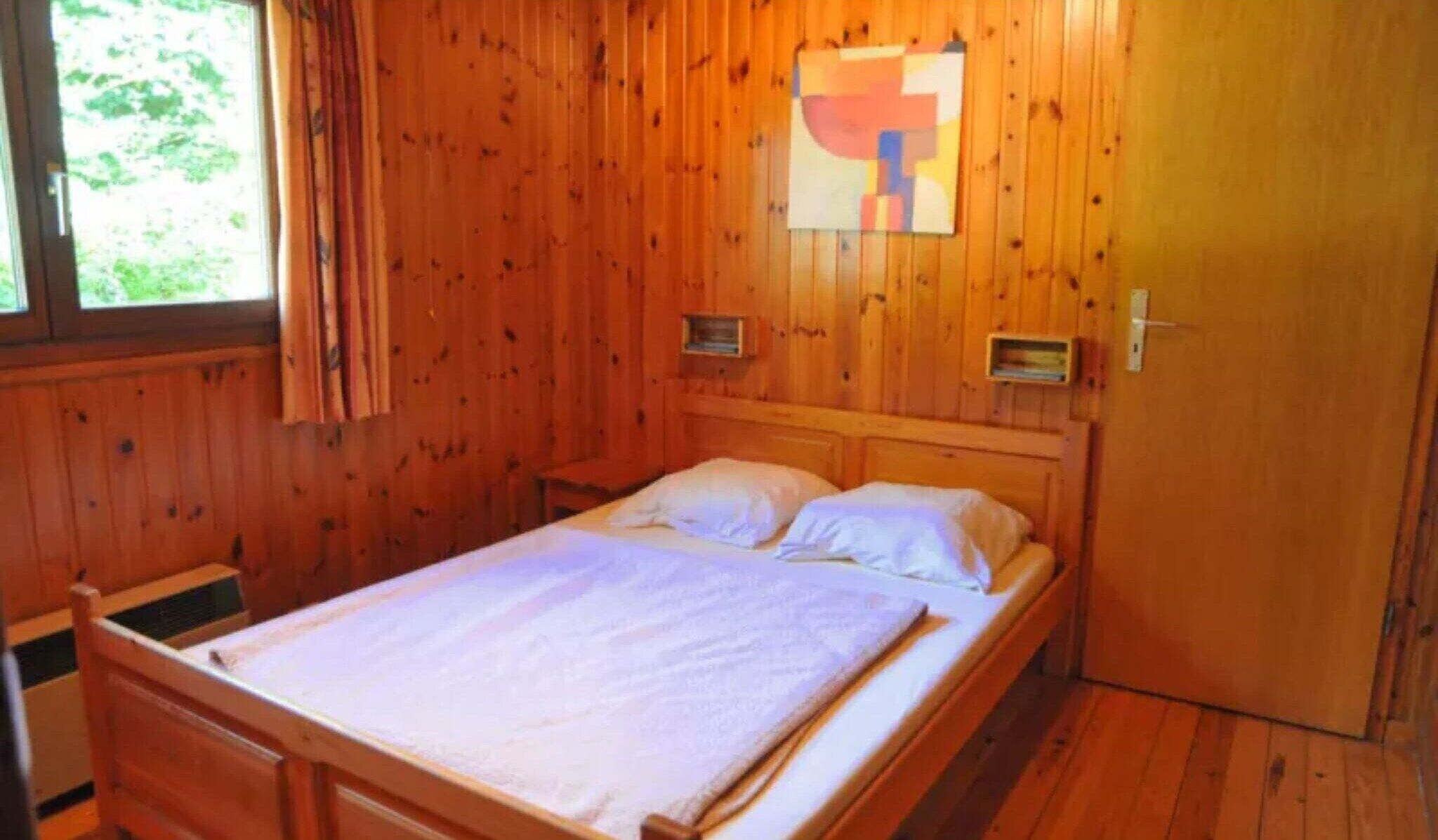Una habitación de madera con una cama, una ventana con cortinas y una puerta.