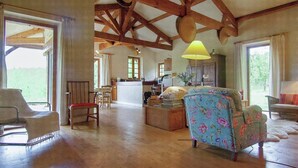 A spacious living room with wooden beams, a dining area, and a kitchen in the background. - Hilltop Home with Valley View (Bouzic)