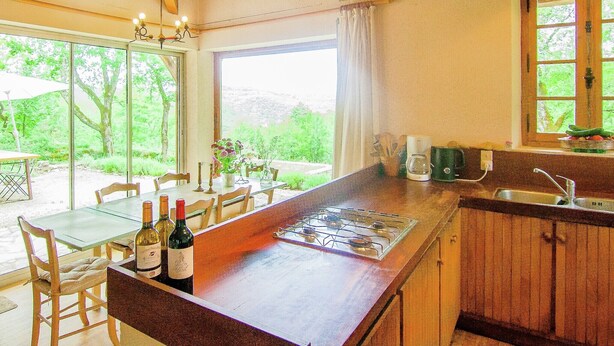 A kitchen with a large island, wooden cabinets, and a window overlooking greenery. - Hilltop Home with Valley View (Bouzic)