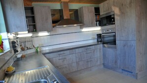 Una cuina moderna amb armaris grisos, electrodomèstics d'acer inoxidable i una llum d'encoixinat a la paret.