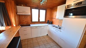 Eine kleine Küche mit Holzwänden, einem eingebauten Herd, einem Spülbecken und einem Kühlschrank.
