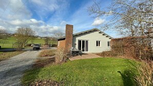 Ein einstöckiges Haus mit Backsteinkamin, überdachter Terrasse und Schotterauffahrt.