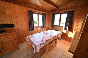 Een kamer met houten lambrisering, een tafel gedekt voor twee personen, een klein kastje en een televisie op een standaard.