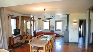 A spacious living area with a wooden dining table, chairs, a leather sofa, a television, and a large mirror. - Stone House in Durbuy with Sauna & Garden Views (Bonsin)