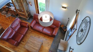 A spacious loft-style living area with a large window, leather sofas, a wooden coffee table, and a bicycle rack. - Stone House in Durbuy with Sauna & Garden Views (Bonsin)